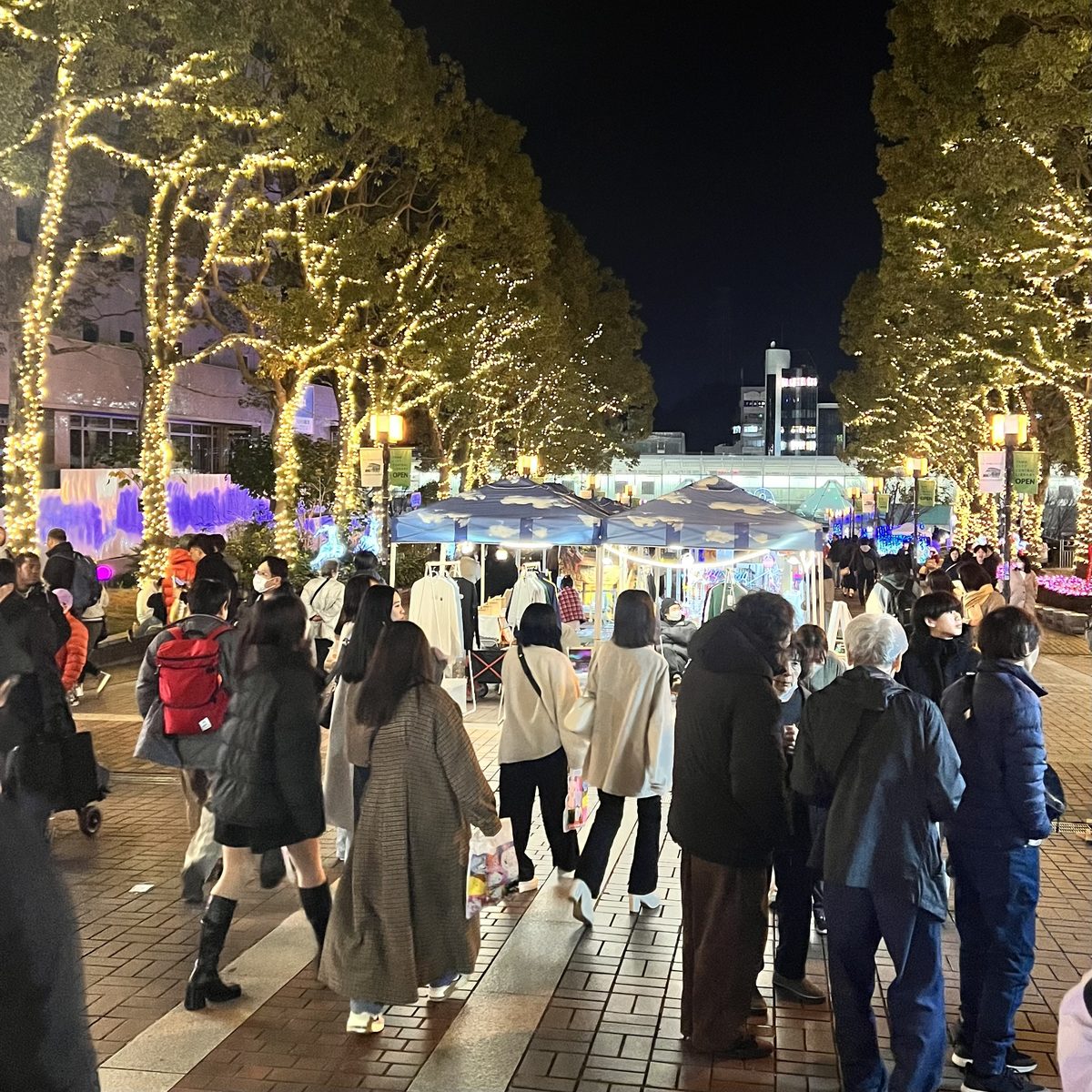 電飾が巻かれた並木の下にテントの店が並び、大勢の人が歩くパルテノン大通りの夜