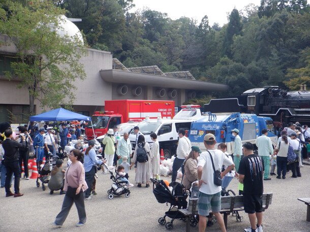 第48回多摩区民祭のはたらく車の展示。消防車、パトカー、清掃車の前にベビーカーを押す家族連れが集まっている