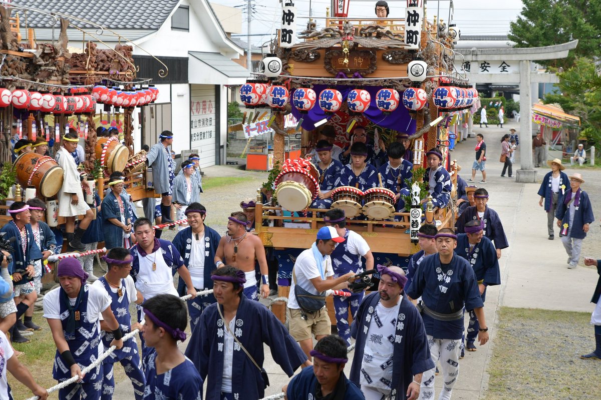 揃いの半纏を着た曳き手が綱を引き、提灯を下げた山車が神社の鳥居の前を進む