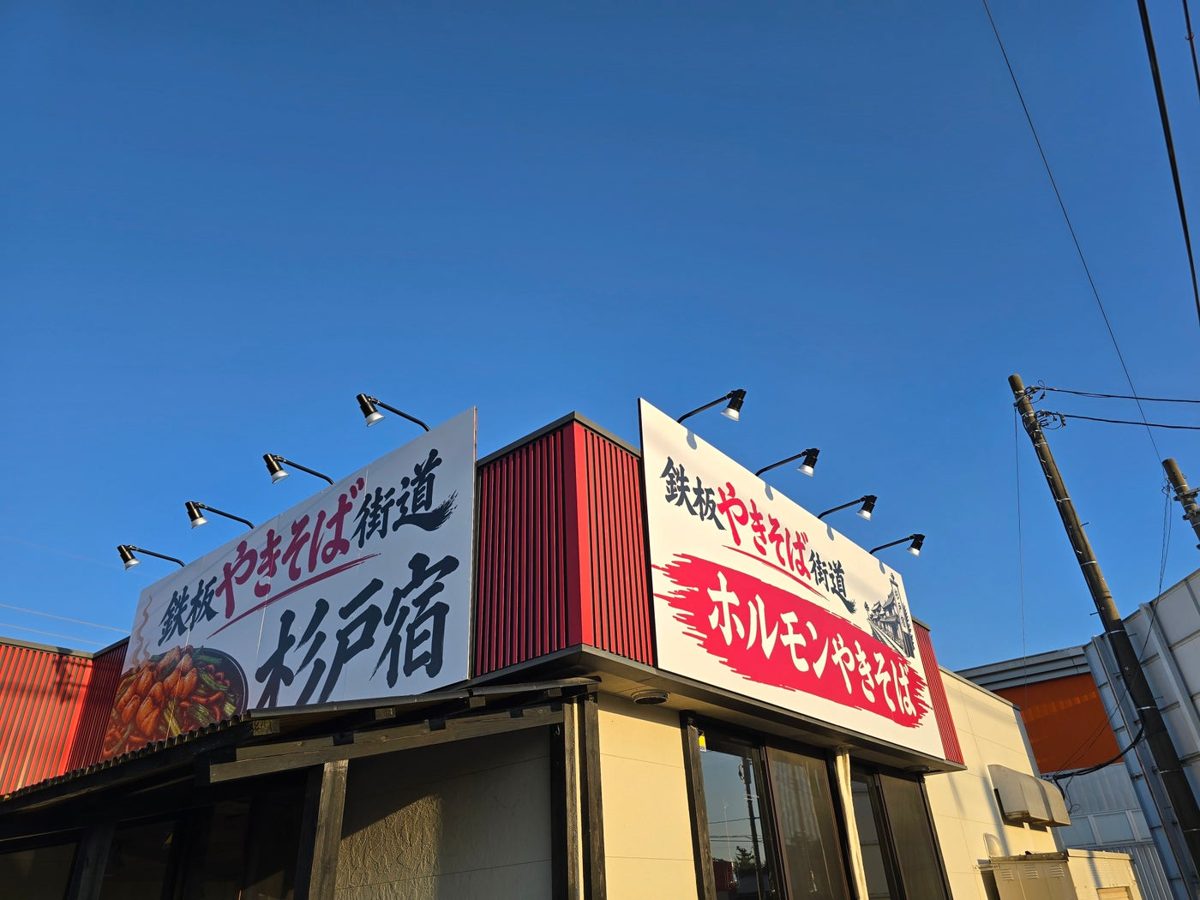 赤い外壁の店舗の屋根の上に「鉄板やきそば街道 杉戸宿」と「ホルモンやきそば」の看板