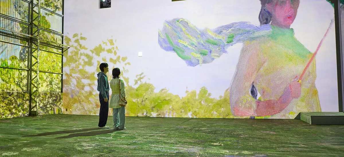 床と壁一面に、日傘をさす女性の絵と緑の草木が投影された空間に、2人が立って見上げている