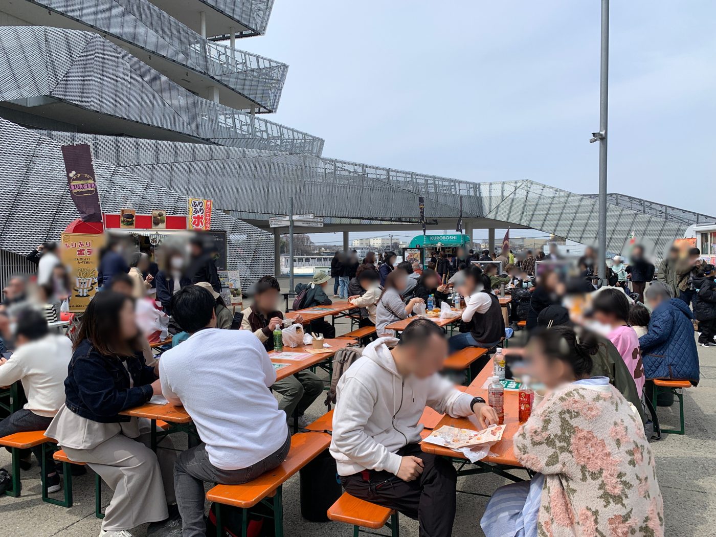 ところざわサクラタウンの中央広場に並ぶテーブル席でパンや飲み物を楽しむ来場者。奥に角川武蔵野ミュージアムの外壁とキッチンカー