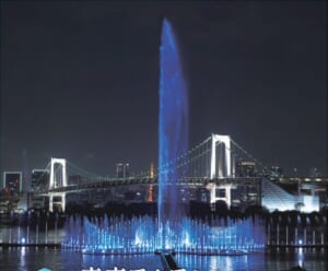 夜のお台場海浜公園で青くライトアップされた高射噴水が高く噴き上がり、手前に横に広がる噴水、背景にレインボーブリッジと東京タワー