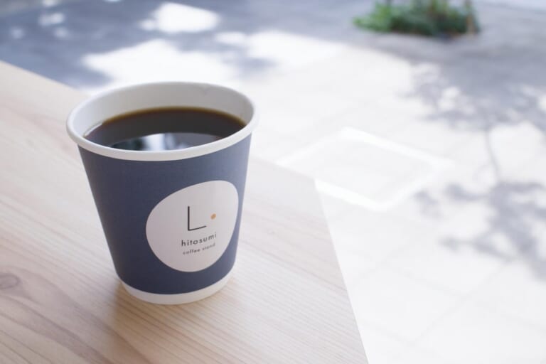 日差しの入る白いテーブルに置かれたhitosumiの青い紙カップのコーヒー