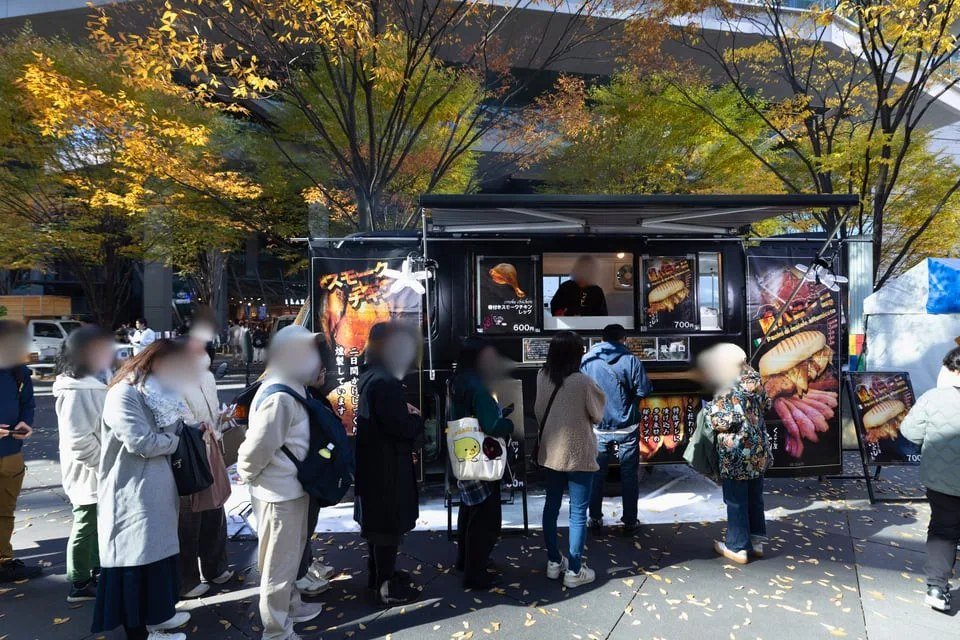 黄葉した木の下に止まった黒いキッチンカーの前に、来場者が列を作っている