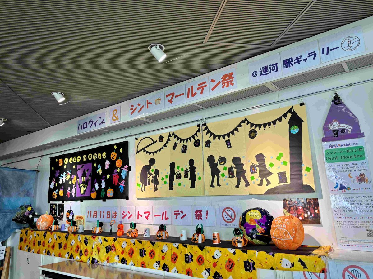 運河駅ギャラリーの展示。「ハロウィン＆シント・マールテン祭」の看板、ランタンを持つ子どものシルエットの切り絵、紙コップのランタンやかぼちゃの飾り、「11月11日はシントマールテン祭！」の掲示