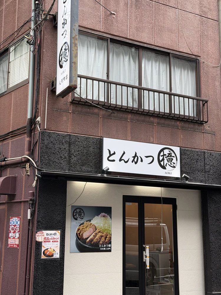 入口の上に「とんかつ 檍 AOKI」の白い看板、2階の壁に縦長の「とんかつ檍 人形町店」の看板が付いた店の外観。入口脇に開店のお知らせが貼られている