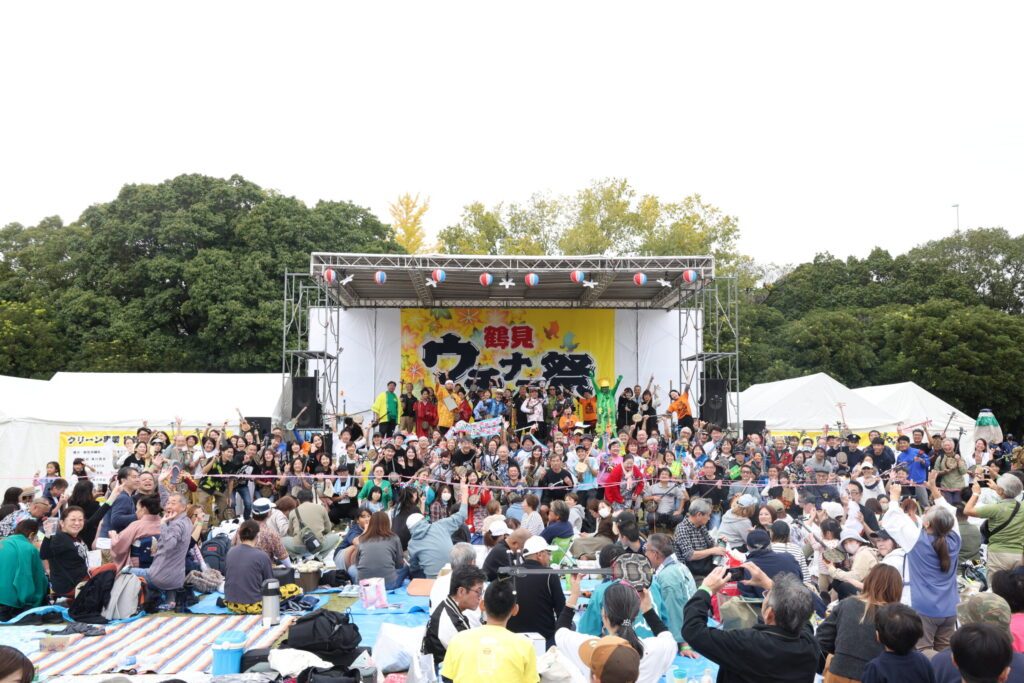 鶴見ウチナー祭のメインステージ前に大勢の来場者が集まり、ステージ上と客席で手を挙げている