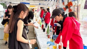 全国梅酒まつりの飲み比べ会場。テントの下のカウンターに梅酒の瓶が並び、スタッフが来場者に注いでいる