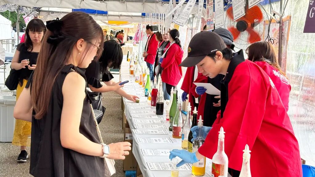 全国梅酒まつりの飲み比べ会場。テントの下のカウンターに梅酒の瓶が並び、スタッフが来場者に注いでいる