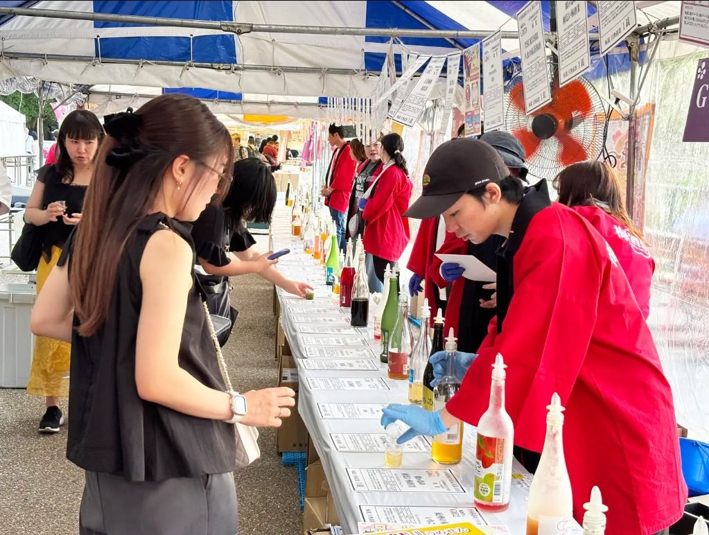全国梅酒まつりの飲み比べ会場。テントの下のカウンターに梅酒の瓶が並び、スタッフが来場者に注いでいる