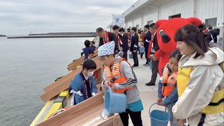 ライフジャケットを着た子どもたちが岸壁から稚魚を放流する様子