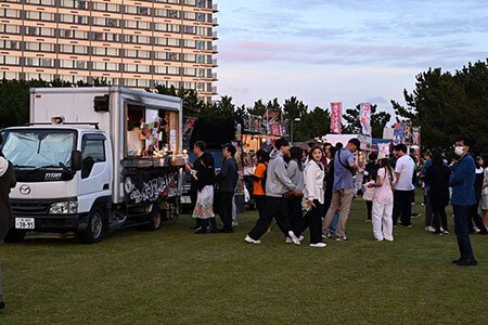 2025年の浦安市花火大会の観覧会場に出たキッチンカーと、芝生に並ぶ来場者