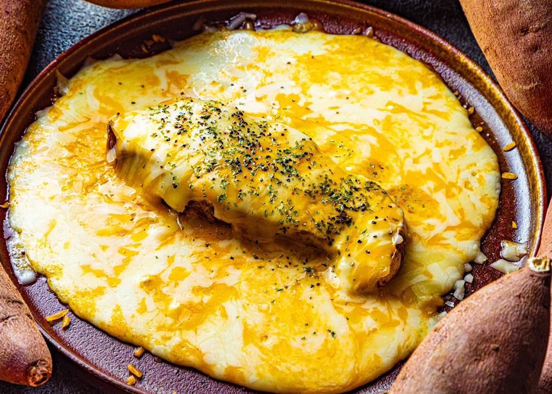 皿いっぱいに広がる溶けたチーズの上に、焼き芋をのせてハーブを振った料理