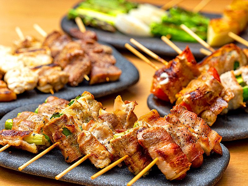 黒い皿に盛られたやきとん串、肉巻きトマト串、ネギ串など