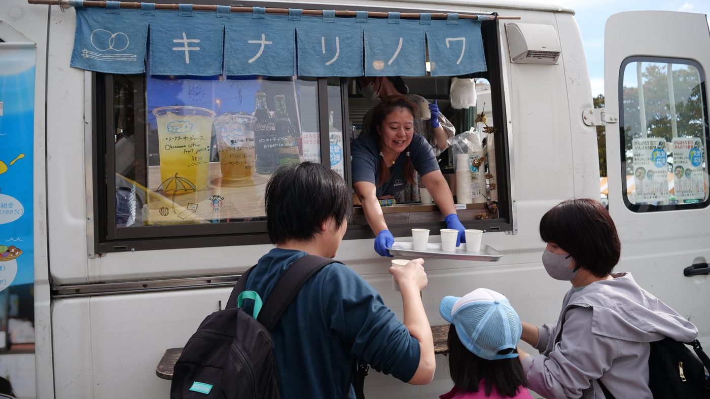 キッチンカーの窓口でスタッフが来場者にカップを手渡している様子