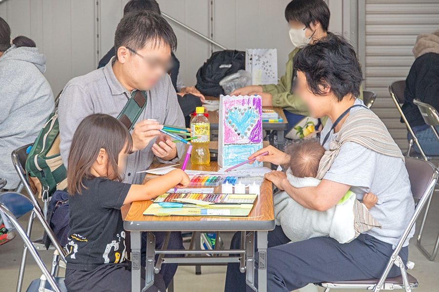 長机で色鉛筆やペンを使い、紙袋に絵を描く親子。机の上にハート模様を描いた紙袋