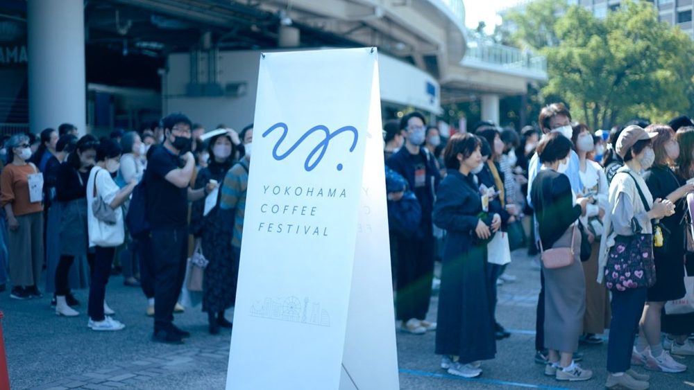 イベントの看板の横に、多くの来場者が並んでいる