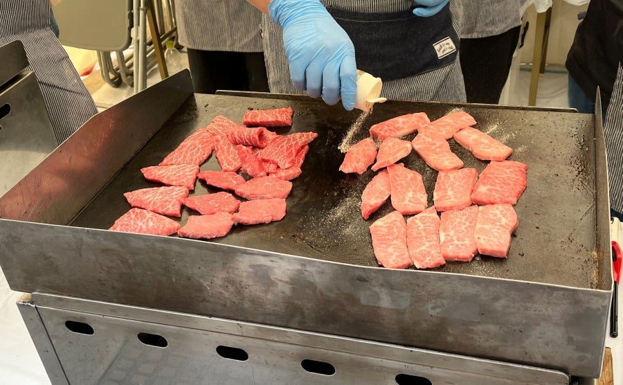 鉄板に霜降りの牛肉が並べられ、スタッフが塩をふっている