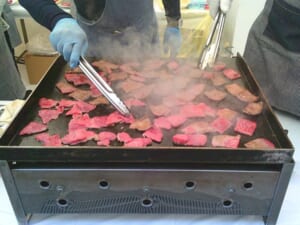 手袋をしたスタッフが鉄板の上で薄切りの牛肉をトングで焼いている