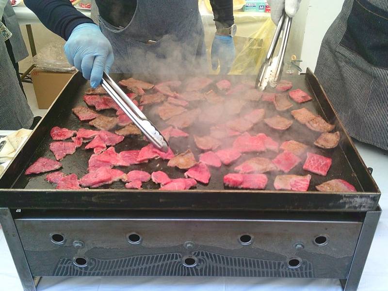 手袋をしたスタッフが鉄板の上で薄切りの牛肉をトングで焼いている
