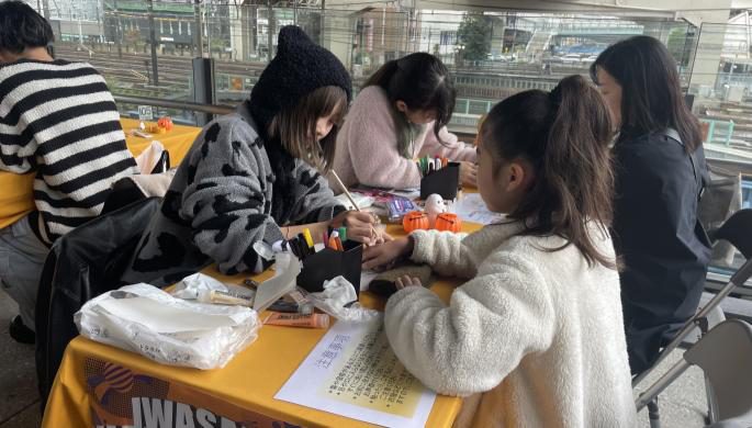 前年のヨコハマ西口ハロウィンで、岩崎学園の幕が掛かったテーブルで工作をする子どもたち