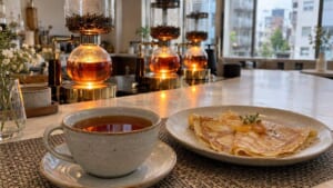 明るい石のカウンターに並ぶ紅茶のサイフォンと、グレーのカップの紅茶、折りたたんだクレープのイメージ画像