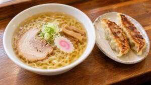透き通った醤油スープに平打ちの縮れ麺、チャーシュー、メンマ、ナルト、ネギをのせたラーメンと、大きな焼き餃子2個のイメージ画像