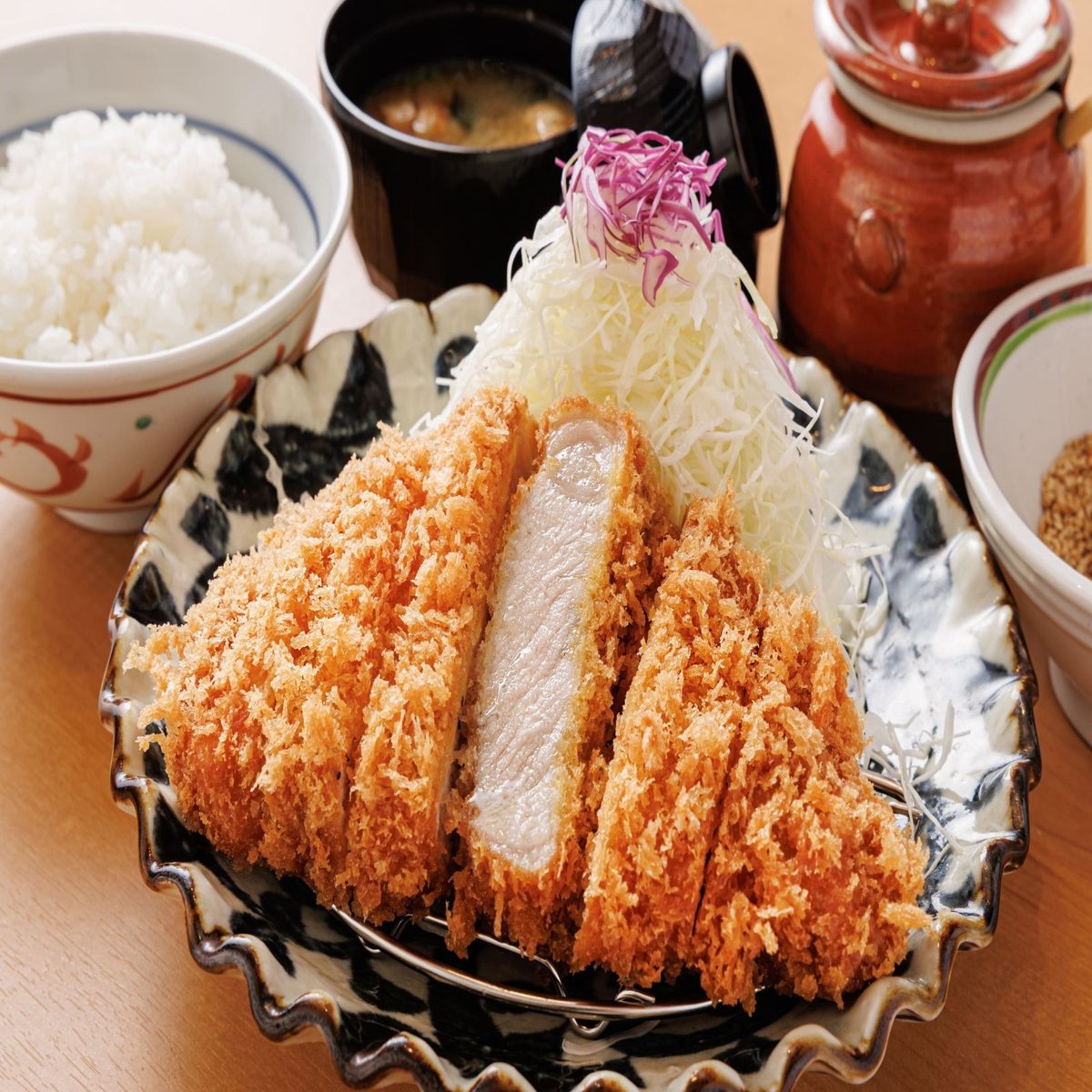 切り分けた厚切りロースかつと千切りキャベツ、白いごはん、味噌汁、漬物の壺が並ぶご膳