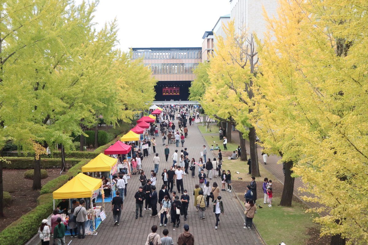 黄色く色づき始めたイチョウ並木の通路に、黄色と赤のテントの模擬店が並び、来場者が歩いている様子
