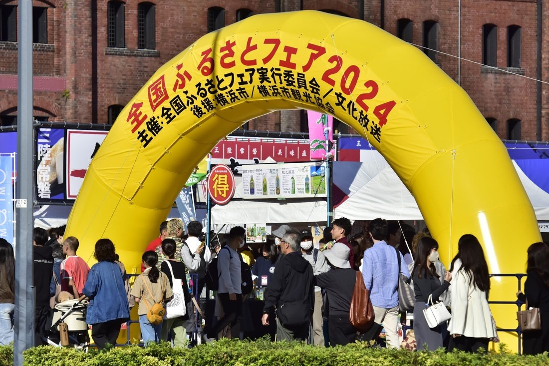 「全国ふるさとフェア2024」と書かれた黄色いアーチの下を、多くの来場者が行き交う赤レンガ倉庫前の会場入口