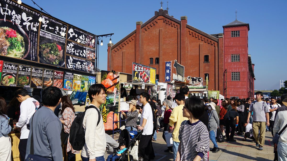 赤レンガ倉庫を背に、沖縄そばなどの看板を掲げたキッチンカーが並び、来場者が行き交う